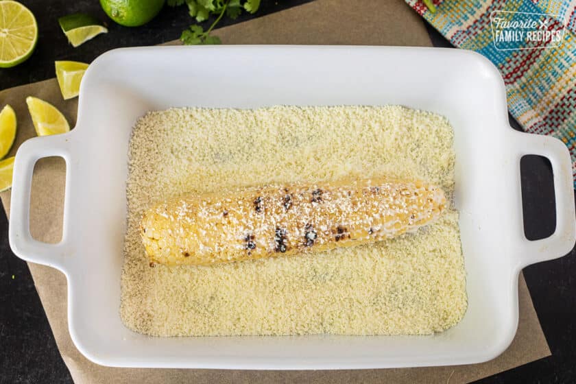 Rolling grilled corn in dish of cojita cheese.