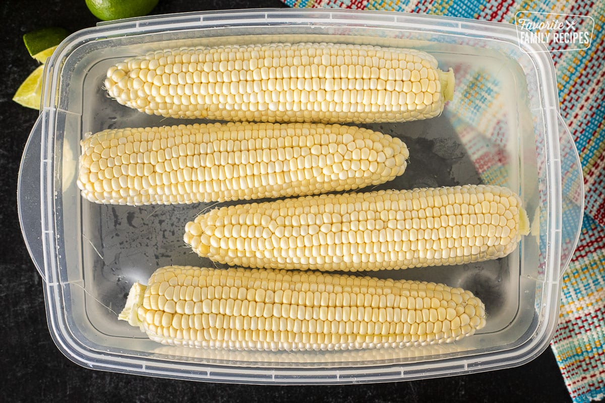 Container with four husked cobs of corn in water.