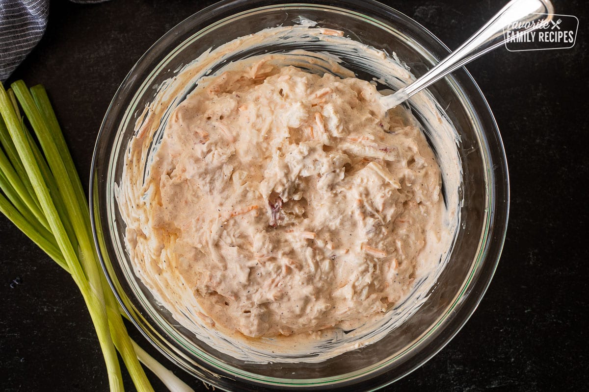 Glass bowl with Hot Crab Dip mixing with spoon.