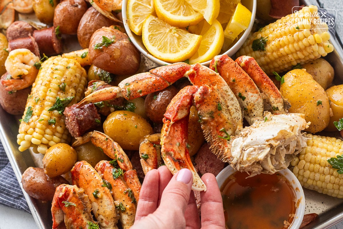 Hand grabbing a crab claw from the sheet pan of crab boil.