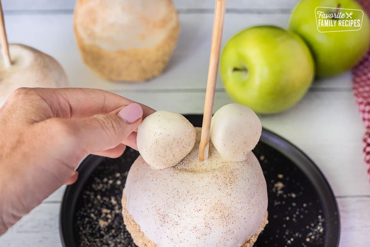 Placing marshmallow ears on an Apple Pie Caramel Apple.