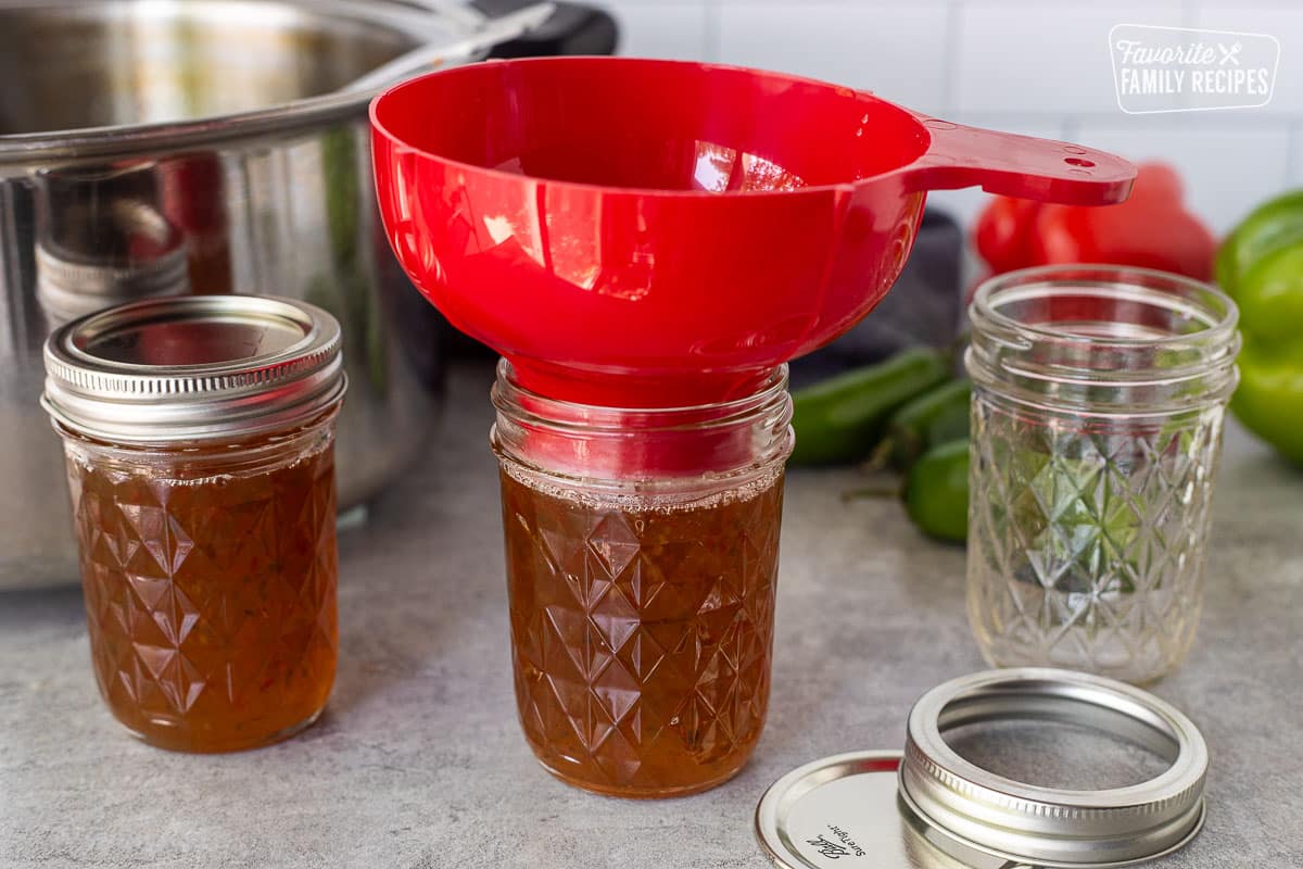 Filling canning jars with jalapeño pepper jelly using a funnel.