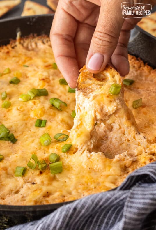 Dipping a slice of bread into skillet of hot crab dip.