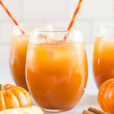 A glass of pumpkin juice with ice and a straw