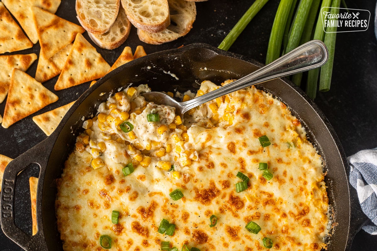 Corn cheese in a skillet with green onions and a spoon resting in the dish.