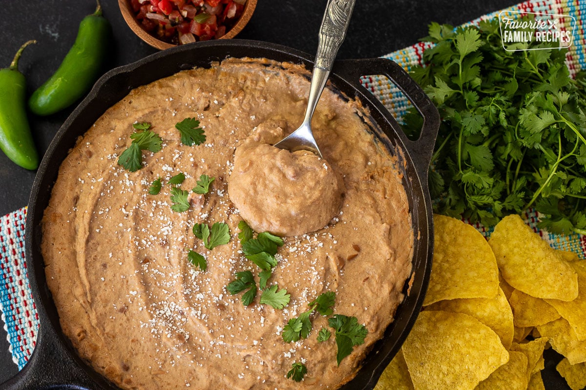 Skillet of Cheater Refried Beans with cilantro and cojita cheese. Spoon resting in the skillet.