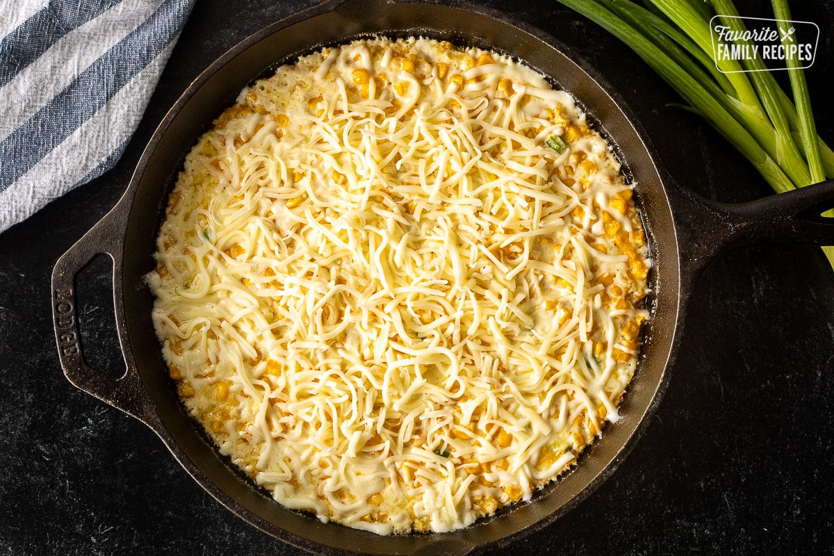 Skillet with hot corn cheese and shredded mozzarella cheese on top.