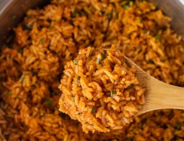 Wooden spoon with Mexican Rice held over a saucepan.