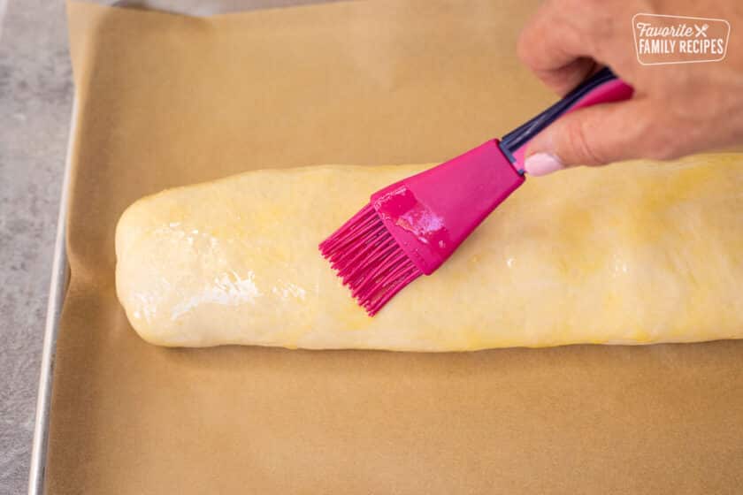 Brushing egg wash on top of unbaked Stromboli.