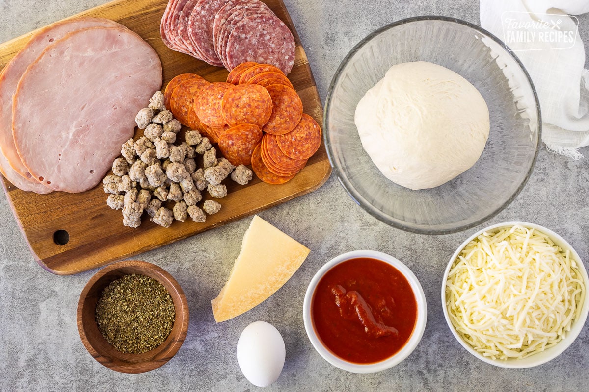 Ingredients to make Stromboli Recipe including dough, mozzarella cheese, pizza sauce, egg, Italian seasonings, parmesan, sausage, salami, pepperoni and deli ham.