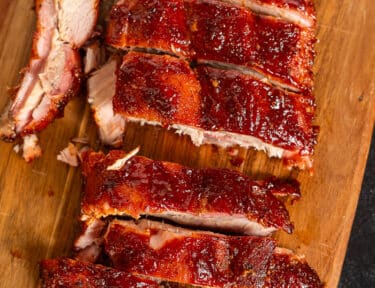 Cut pieces of Smoked Ribs on a cutting board with a knife.