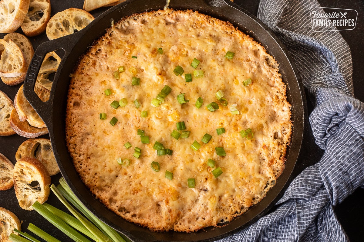 Baked Hot Crab dip in a skillet with green onion on top. Bread slices on the side.