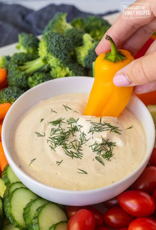 Dipping a yellow bell pepper into a bowl of veggie dip.