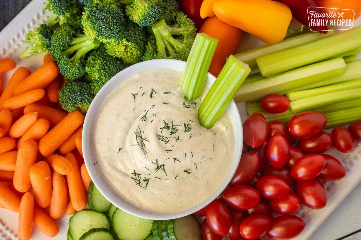 Veggie dip with two sticks of celery. Surrounded by other vegetables.