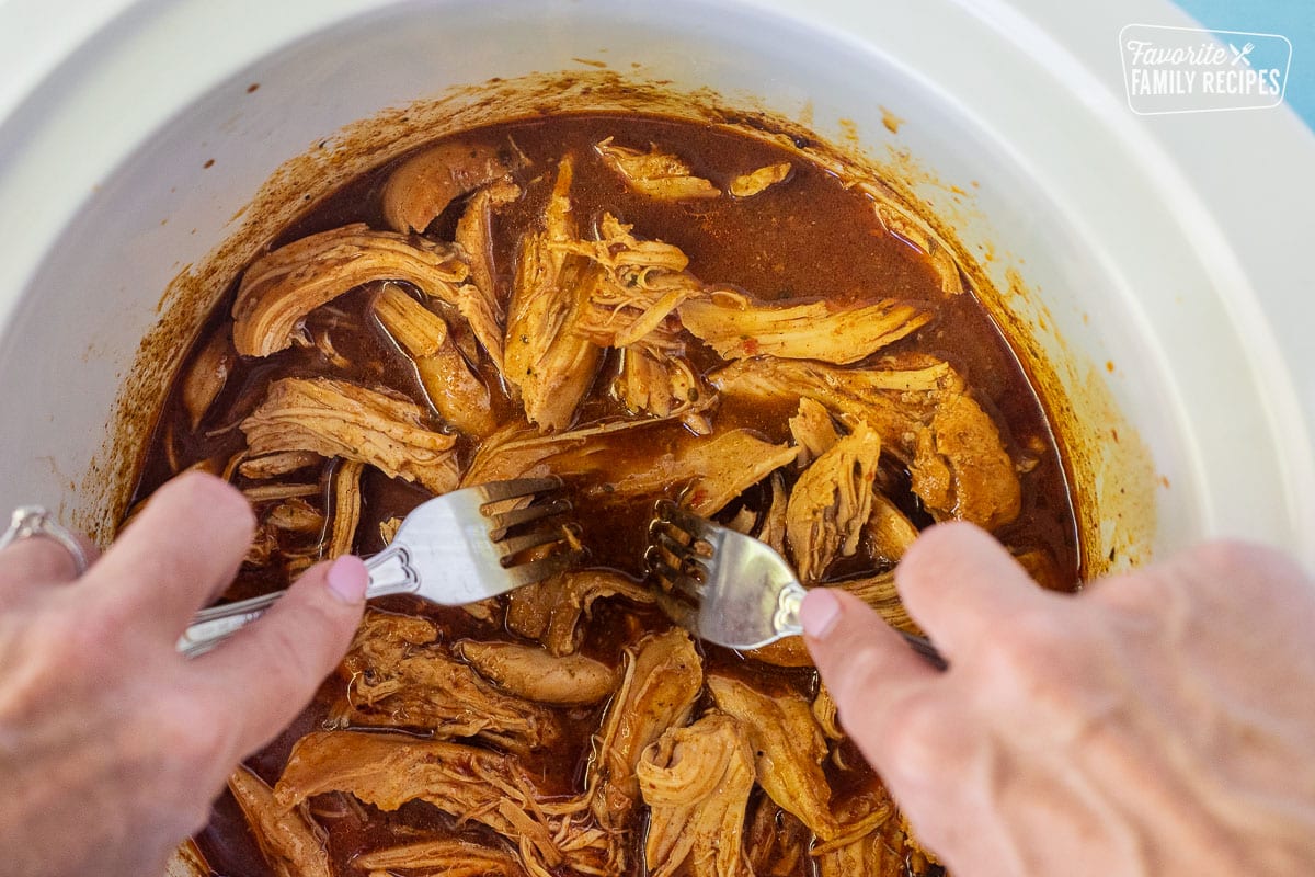 Shredding Mexican Shredded Chicken in a crock pot with forks.