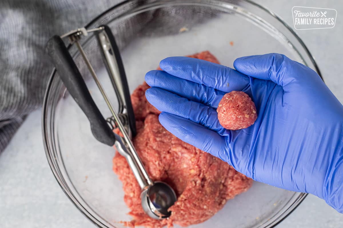 Hand holding a round shaped meatball over a bowl of mixture.