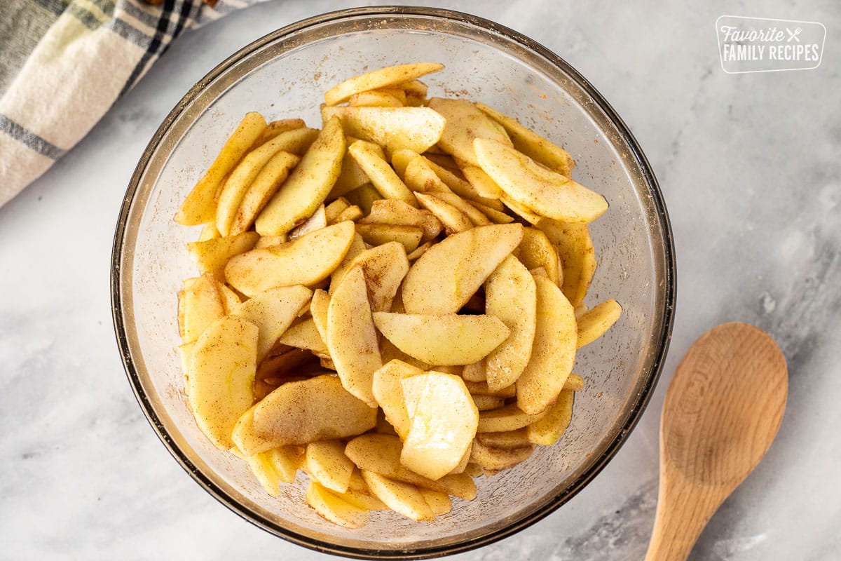 Mixing bowl of sliced apples covered in cinnamon sugar mixture for Apple Crisp.