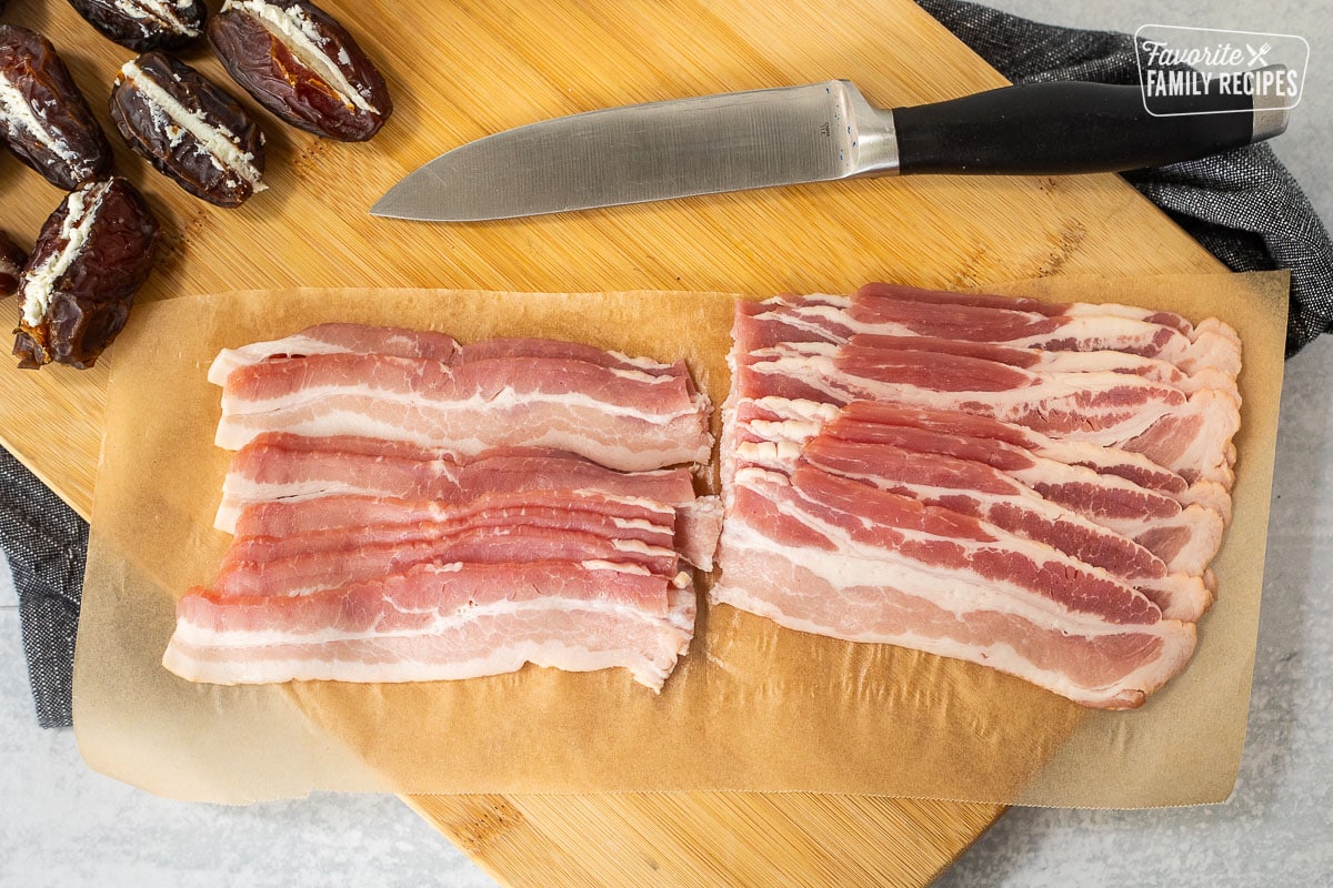 Slices of bacon cut in half on a cutting board.