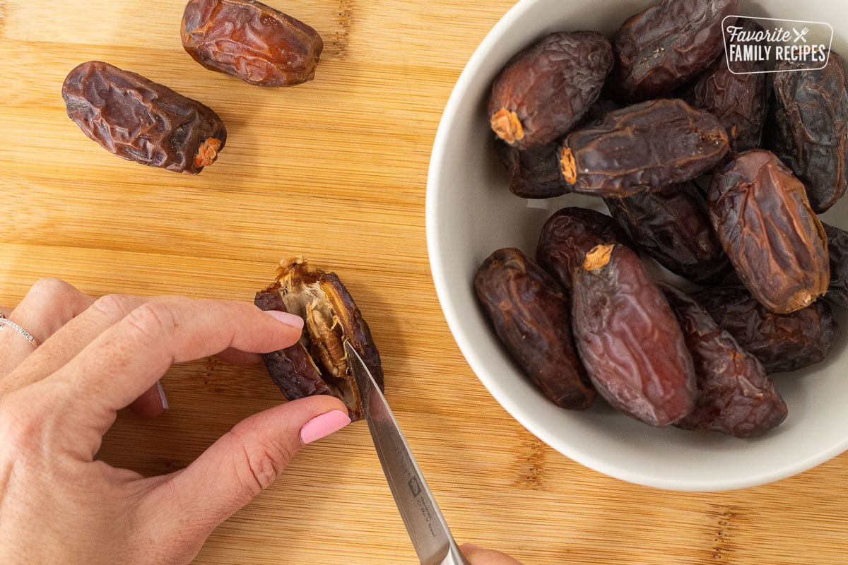 Cutting into a date with a small knife next to a bowl of dates.