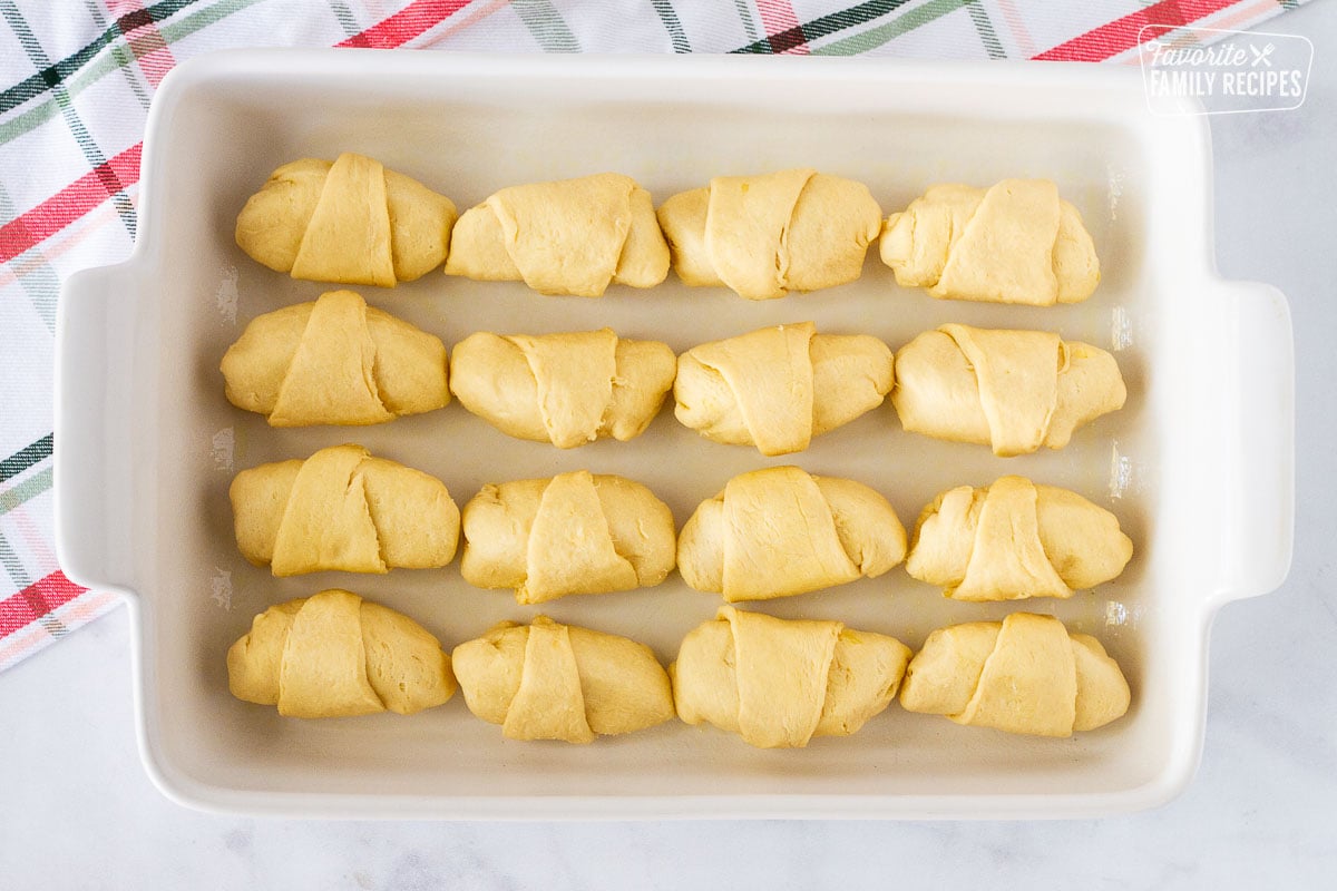 Twelve rolled Apple Dumplings ins a baking dish.