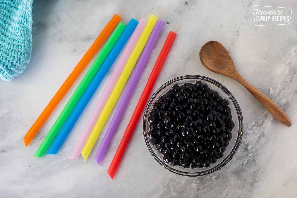 Black tapioca pearls in a bowl with a spoon and large colorful straws on the side.