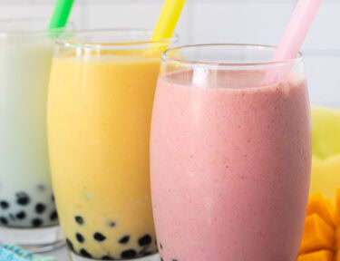 Strawberry, honeydew melon and mango boba smoothies in glasses with colorful large straws.