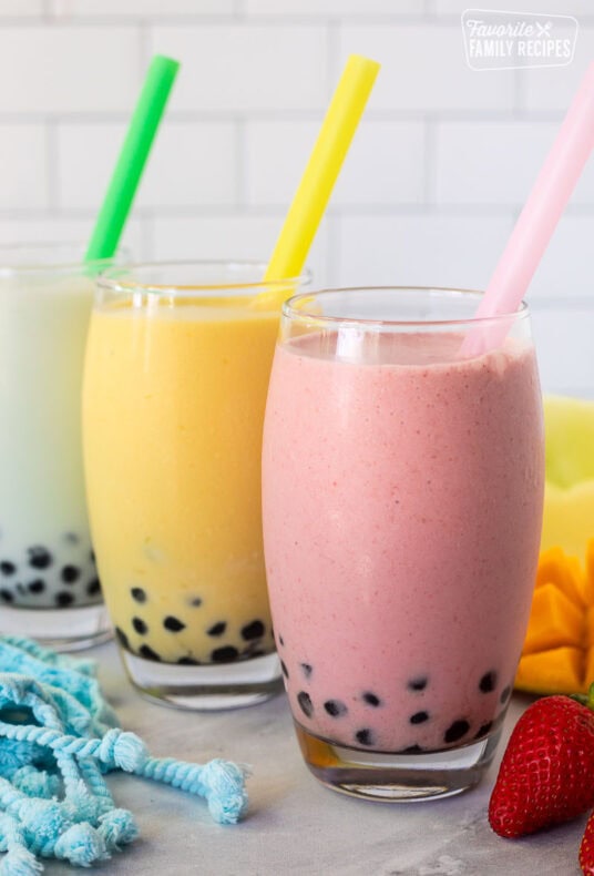 Strawberry, honeydew melon and mango boba smoothies in glasses with colorful large straws.