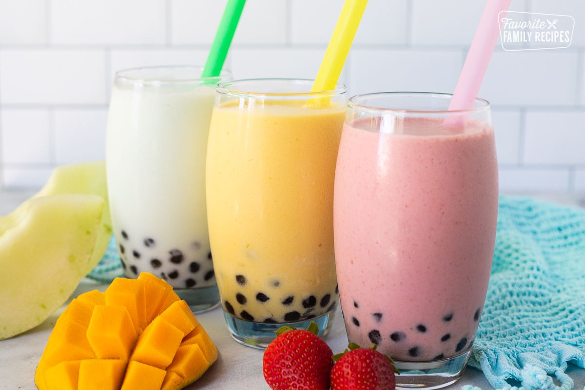 Lined up strawberry, honeydew melon and mango boba smoothies in glasses with colorful large straws.