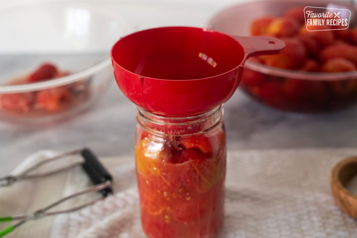 Canning funnel over a canning jar of tomatoes.