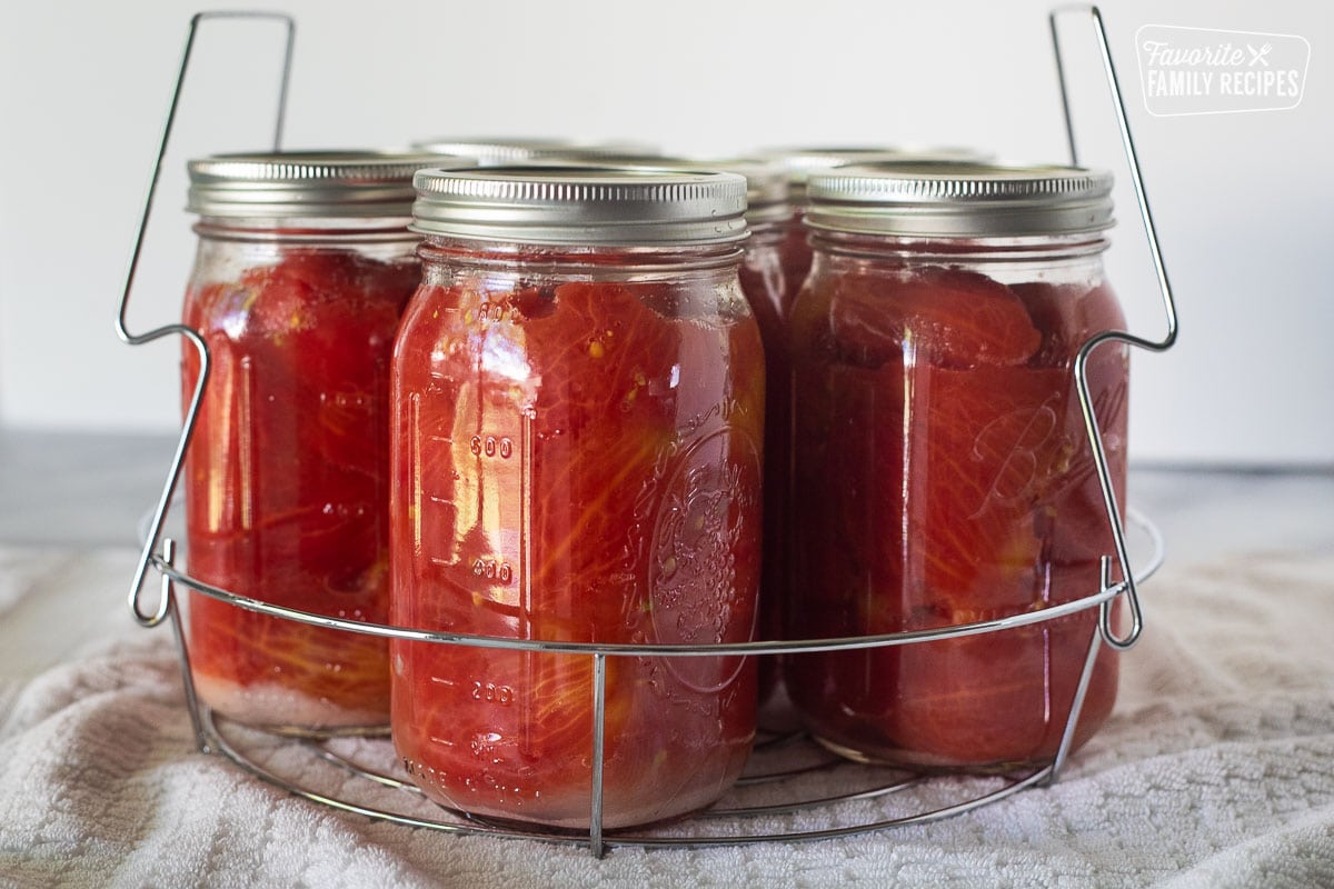 Canning jars with tomatoes on a canning rack.