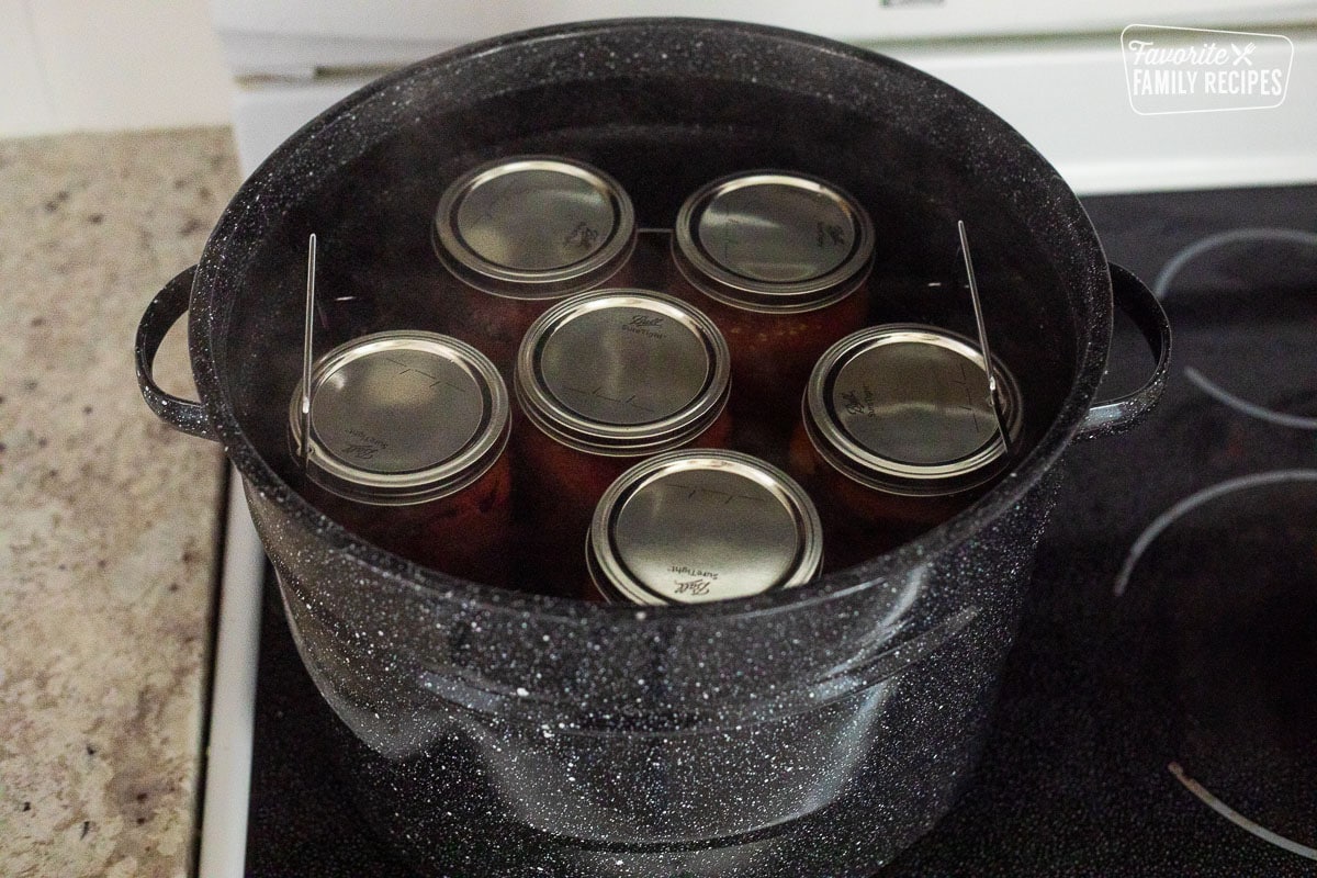 Canning jars with tomatoes in a canning pot of steamy water.