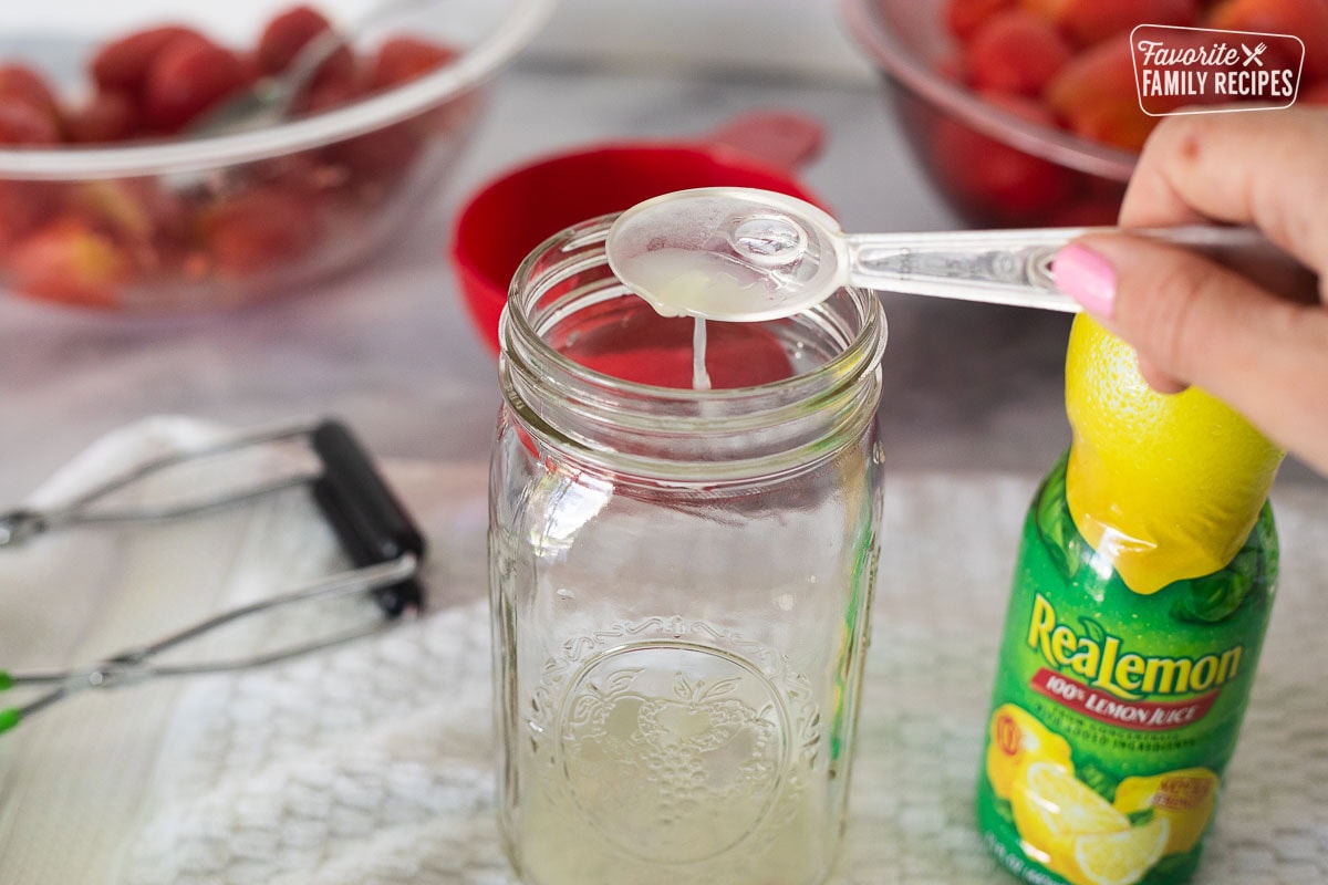 Pouring lemon juice from a tablespoon in a canning jar.