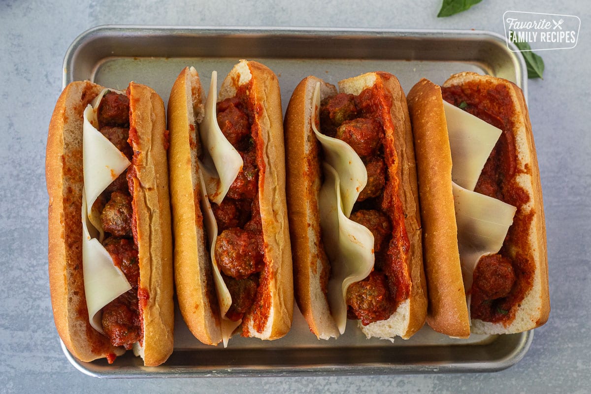 Four Meatball Sandwiches lined up on a baking sheet with unmelted cheese.