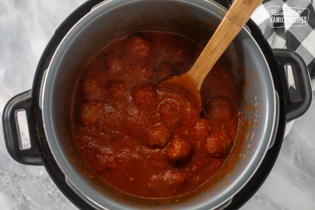 Cooked meatballs in an instant pot with a wooden spoon.