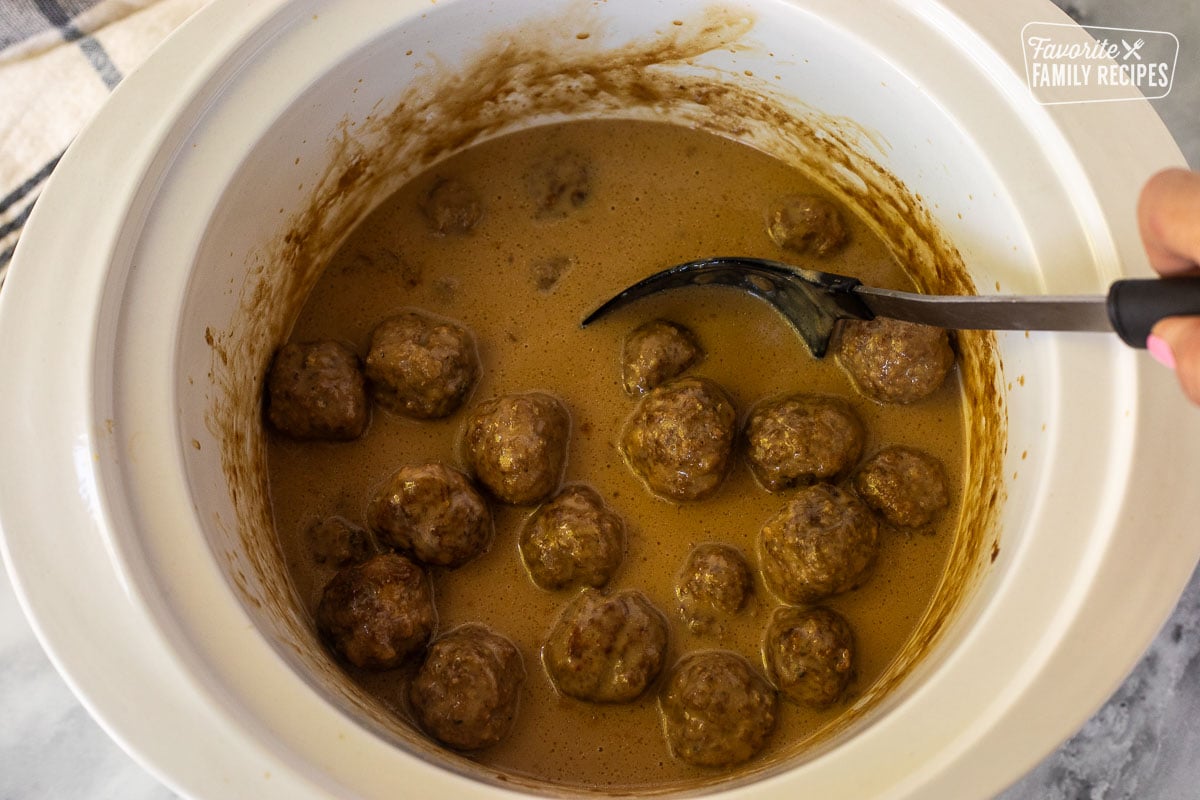 Stirring Crock Pot Swedish Meatballs with a spoon.