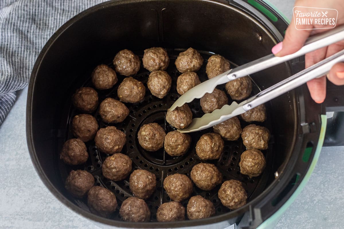 Flipping meatballs with tongs in the air fryer.