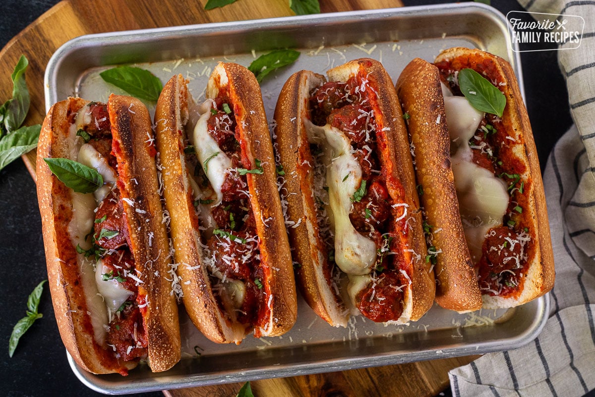 Baking sheet with four baked Meatball Sandwiches with fresh parmesan cheese grated on top and basil.