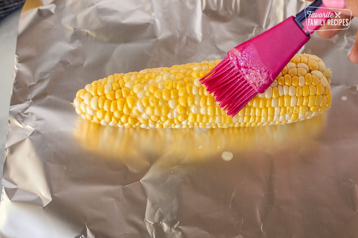 Brushing melted butter on a cob of corn over foil.