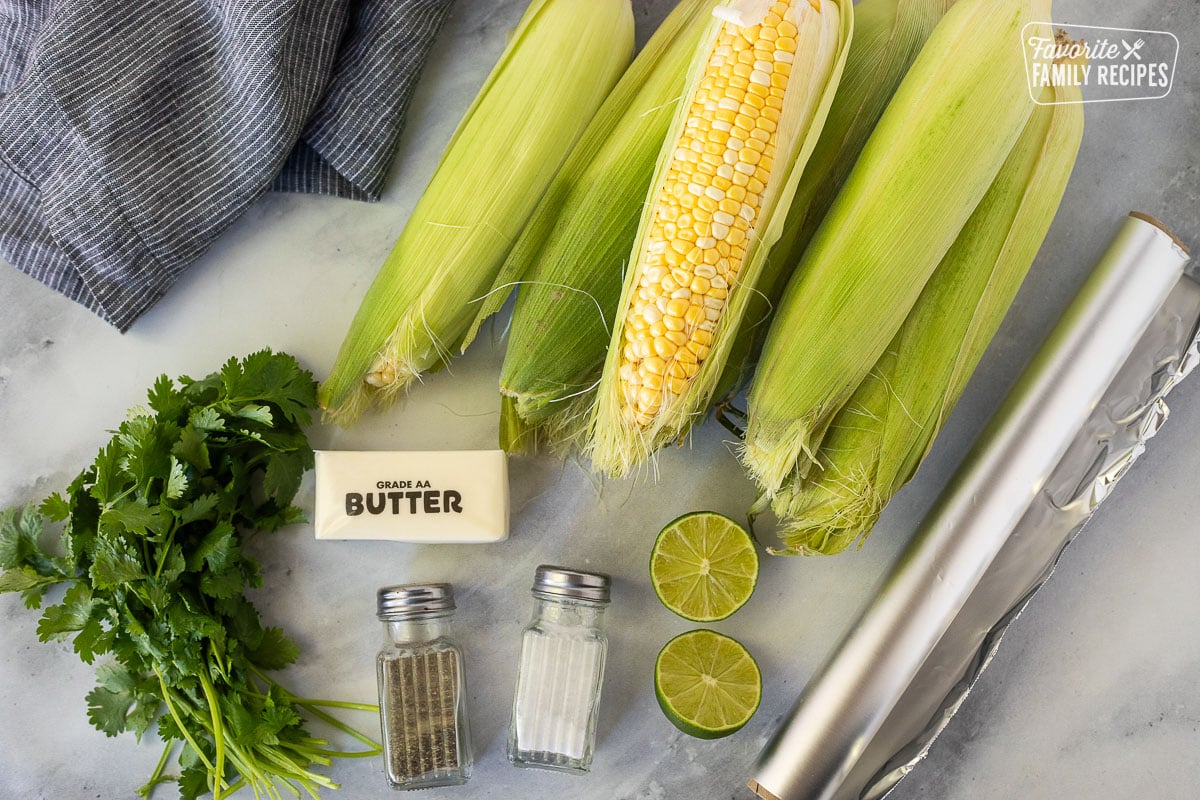 Ingredients to make Grilled Corn on the Cob including corn, cilantro, butter, salt, pepper, lime and foil.