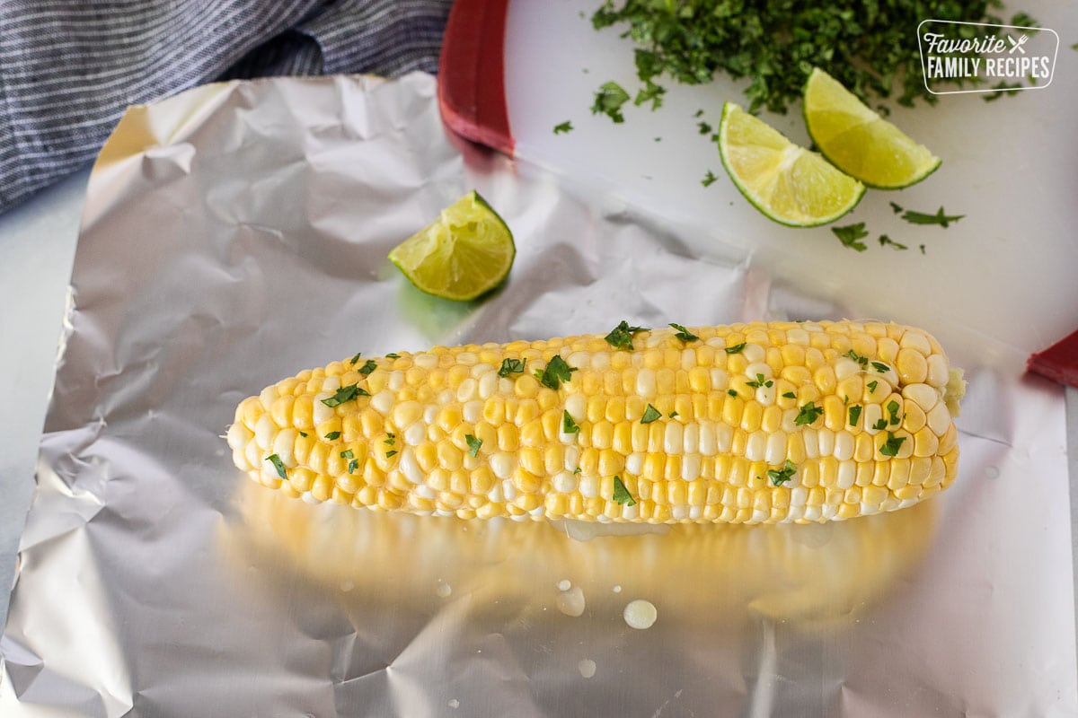 Cilantro sprinkled on cob of corn over foil.