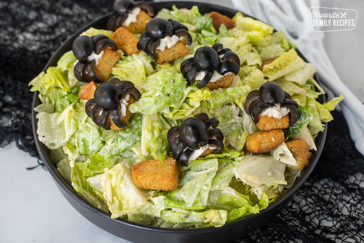 Bowl of Caesar spider salad with black olives shaped like spiders on croutons.