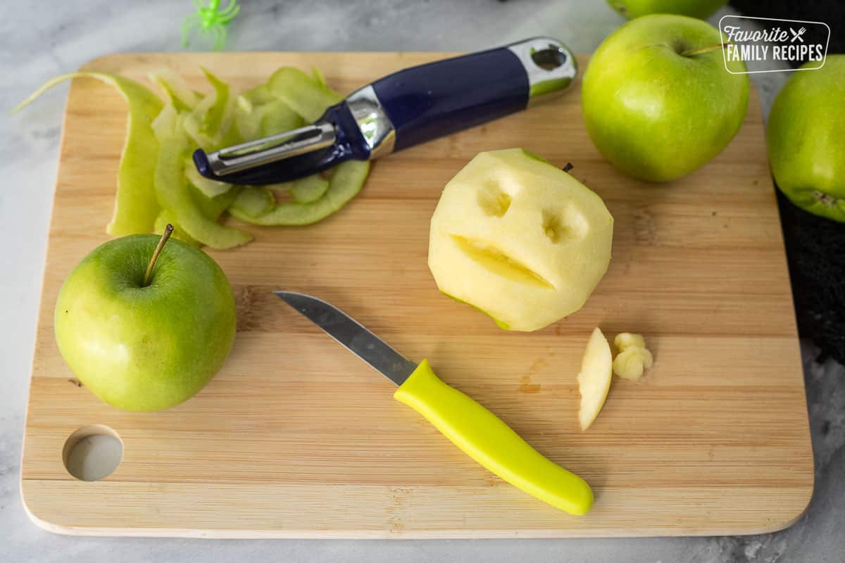 Cutting board with a peeled green apple and face carved out with knife.