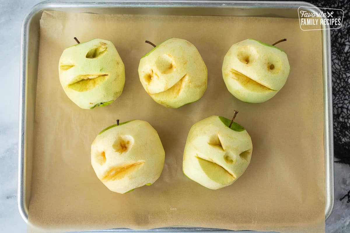 Baking sheet lined with parchment paper and five baked carved apples.