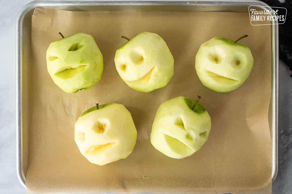 Baking sheet lined with parchment and five carved green apples with stems.