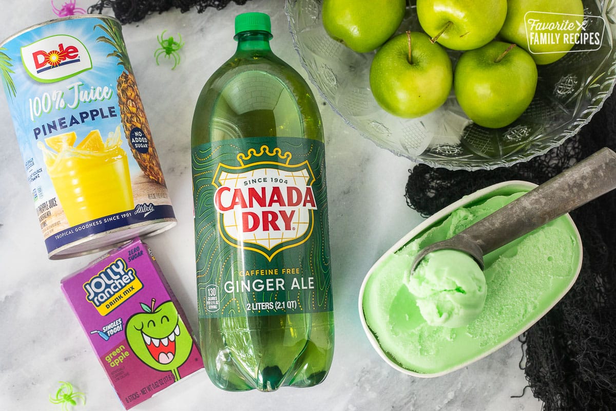 Ingredients to make Halloween Punch including ginger ale, pineapple juice, jolly rancher green apple mix, green apples and lime sherbet.