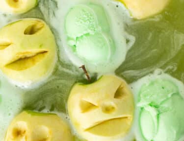 Halloween Punch in a bowl with floating apple heads and scoops of lime sherbet.