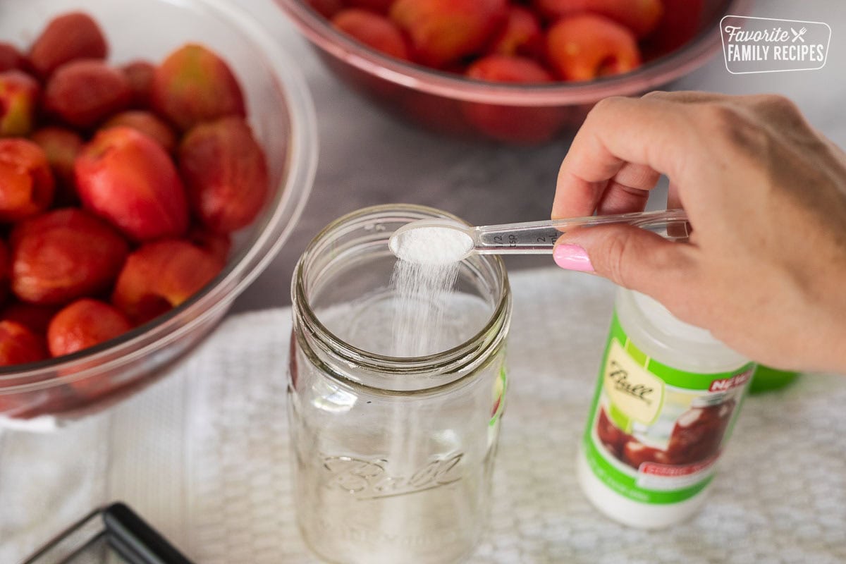 Pouring citric acid in the bottom of a canning jar.