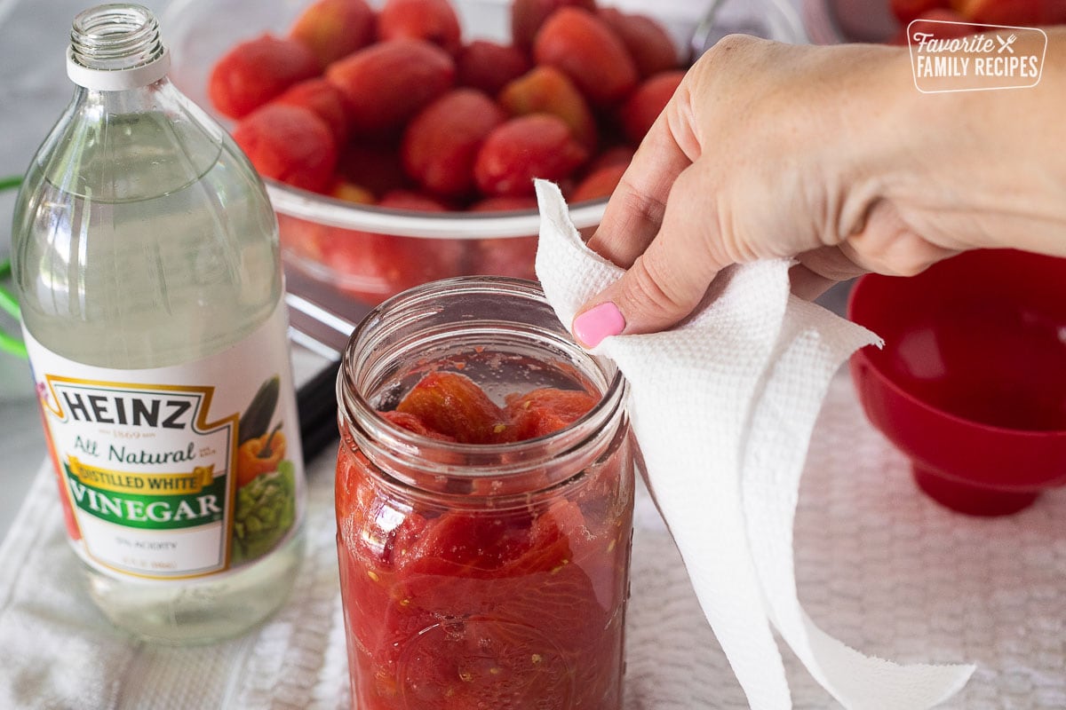 Cleaning the rim of the canning jar with a paper towel and white vinegar.