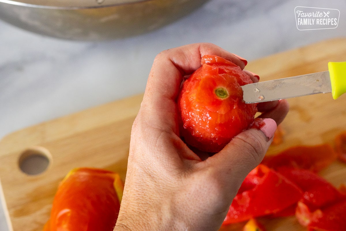 Cutting top off a tomato with a knife.