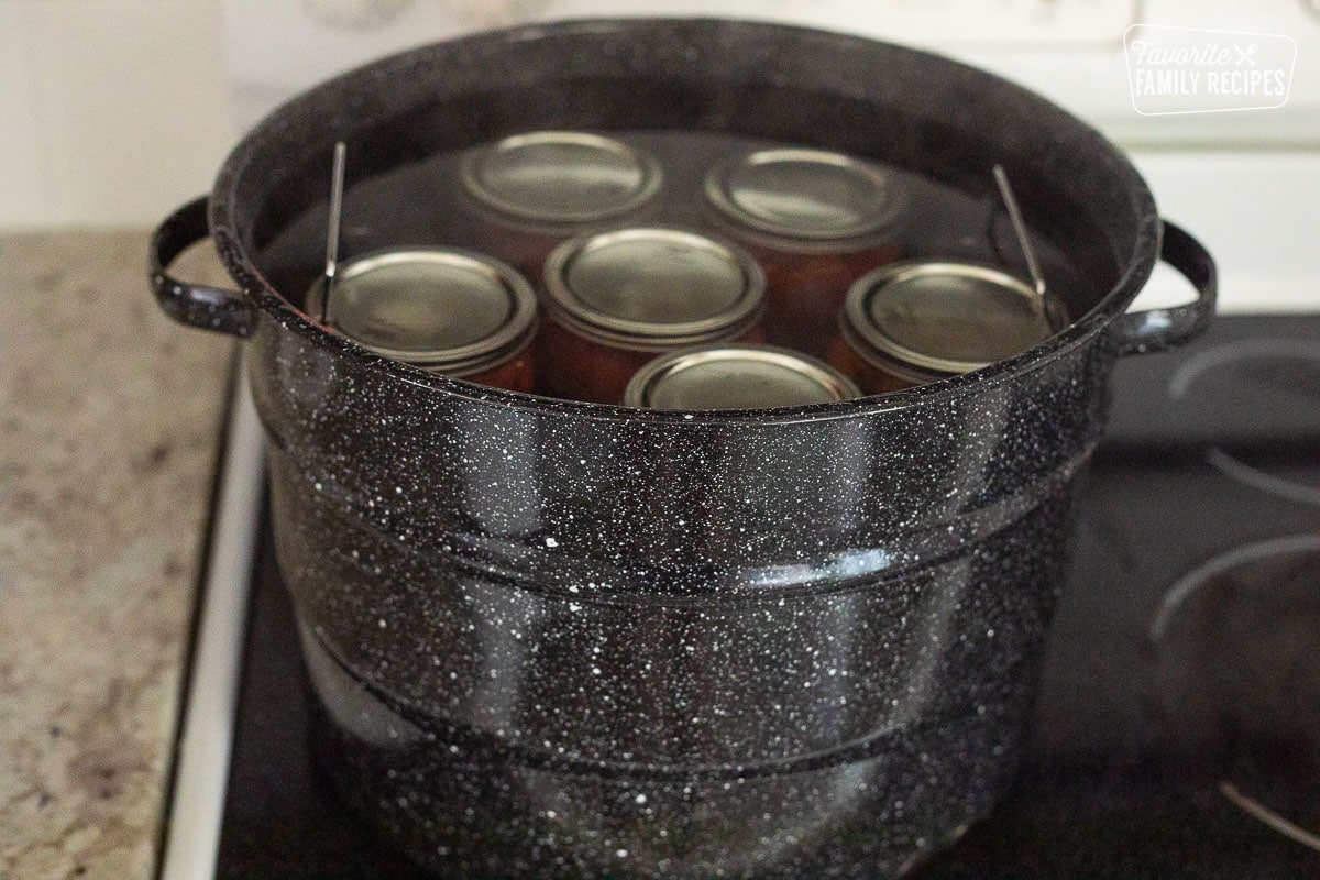 Canning jars of whole tomatoes in a canning pot of steaming water.